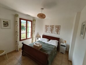 A bedroom with a wooden bed, a window with curtains, a bedside table with a lamp, and wall art. - Le Mas des Oliviers - Swimming pool & Farniente (Sernhac)