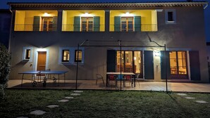 A two-story house with a balcony, a patio with a table and chairs, and a door leading to an interior space.