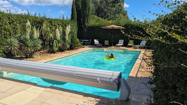 A swimming pool with a person in a float, surrounded by greenery and outdoor furniture.