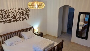 A bedroom with a wooden bed, a wall-mounted tree decoration, a hanging light fixture, and a mirror.