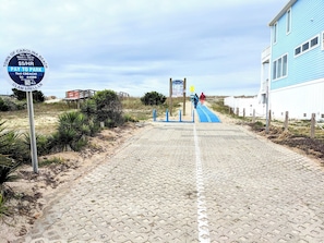 A paved pathway leading to a beach entrance with a parking sign, a blue building, and a wooden structure in the background. - 2nd Row Carolina Beach Cozy 1-bedroom apartment in perfect Carolina Beach (Carolina Beach)