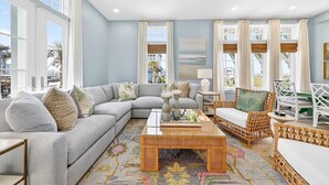 Un salón con un sofá modular, una mesa de centro, muebles de mimbre y ventanas amplias.