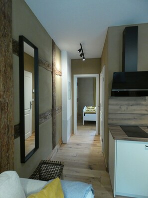 Un pasillo estrecho con una cama, un espejo, una kitchenette y una puerta que da a otra habitación.