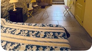 Une pièce avec un plafond en pierre, un lit recouvert d’une courtepointe à motifs floraux, une petite table avec une lampe et une chaise.