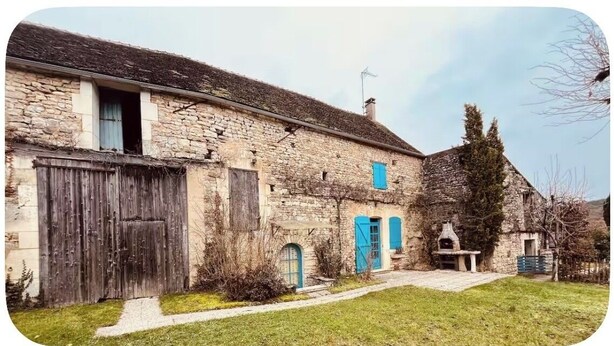 Un bâtiment en pierre avec une porte en bois, un petit porche et une cheminée.