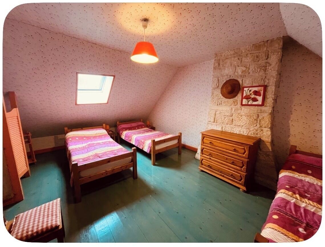 A room with two wooden beds, a wooden dresser, a stone wall, a window, and a hanging light fixture.