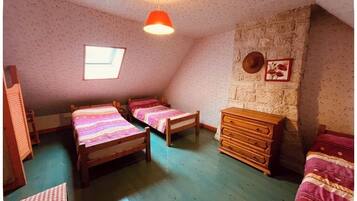 A room with two wooden beds, a wooden dresser, a stone wall, a window, and a hanging light fixture.