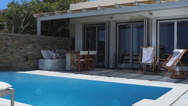Area piscina moderna con muro in pietra, poltrone da relax e patio con vetrate.
