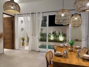 Un comedor con una mesa de madera dispuesta para cuatro personas, rodeada de sillas de mimbre y vistas a un jardín tropical a través de un ventanal.