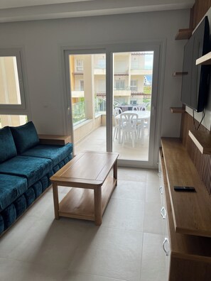 Un soggiorno moderno con un divano, un tavolino e una televisione. Una porta scorrevole in vetro dà accesso a una zona esterna con tavolo e sedie.