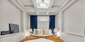 A hotel room with a bed, two bedside lamps, a ceiling light, and a framed picture on the wall.