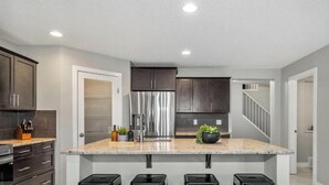 Une cuisine moderne avec des meubles de couleur sombre, des appareils en acier inoxydable, un plan de travail en granit et un îlot central doté de tabourets.