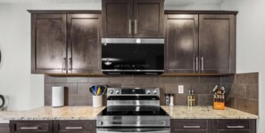 A kitchen with dark cabinets, a stainless steel range hood, a built-in oven, and a granite countertop.