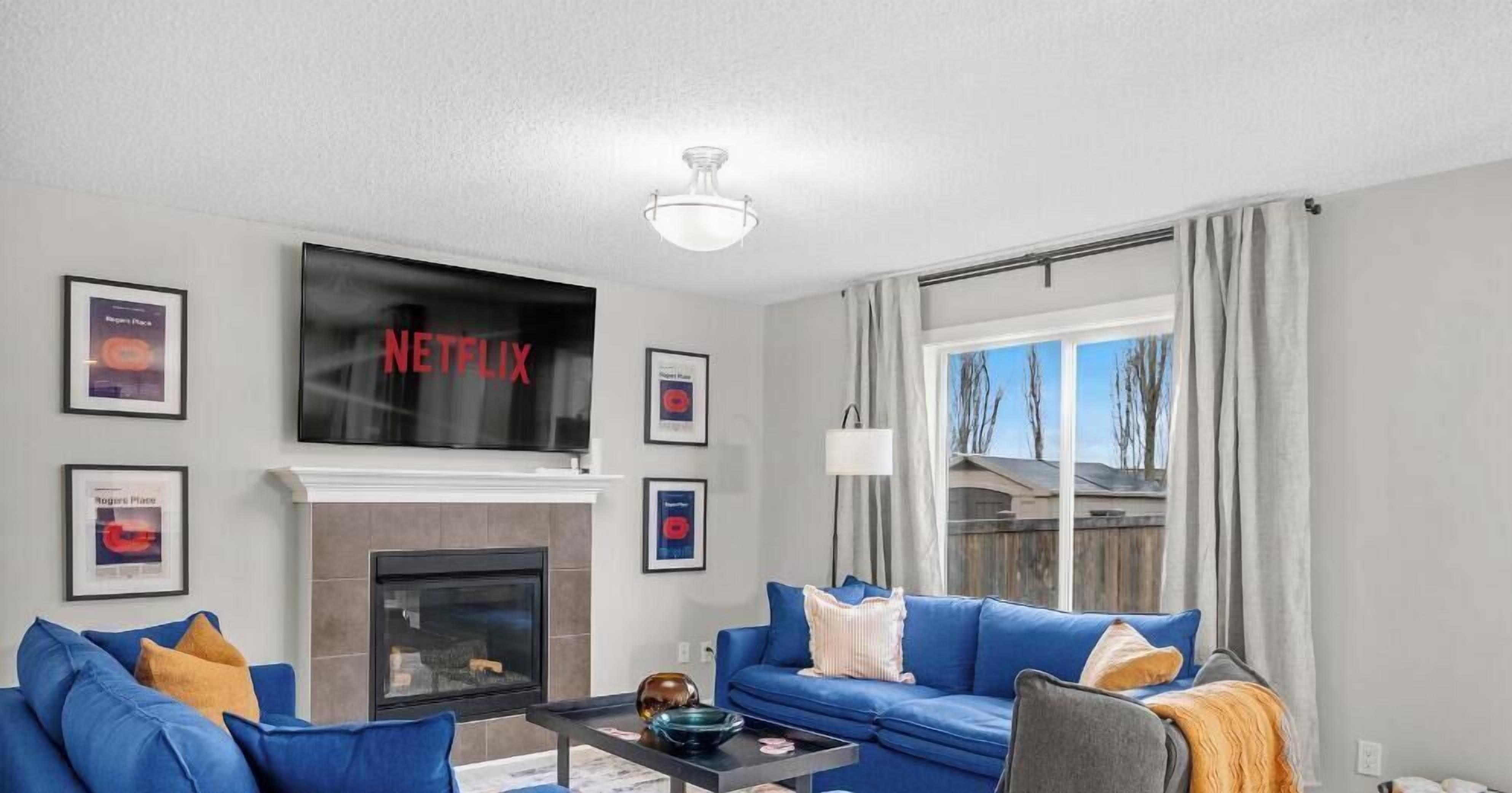 A living room with a fireplace, a flat-screen TV mounted above it, and a large window with curtains.
