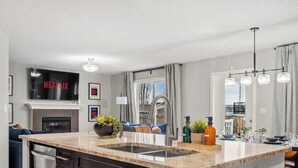 Une cuisine moderne dotée d’un four encastré, d’un grand îlot central avec un évier, et d’un téléviseur à écran plat fixé au-dessus du four, qui affiche le logo « NETFLIX ».