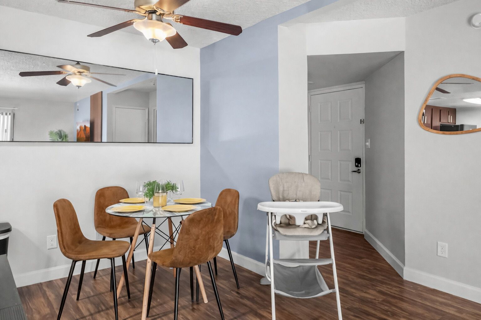 A dining area with a round table, four chairs, a ceiling fan, and a baby high chair.