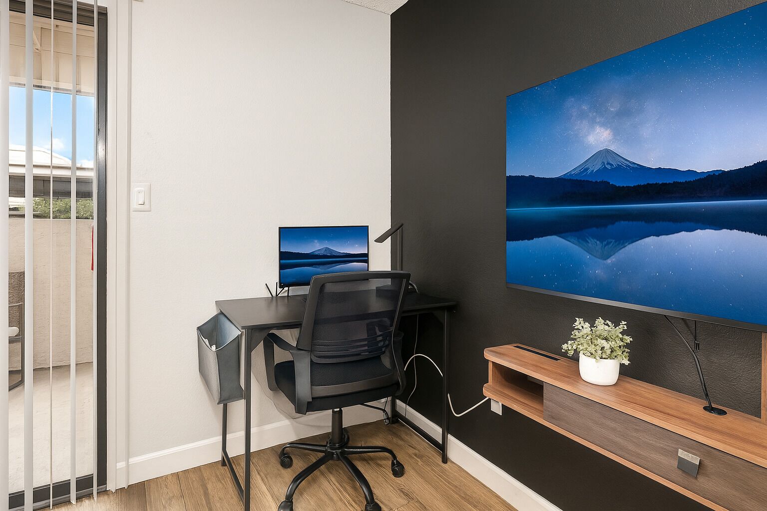 Un espace de bureau moderne comprenant un bureau, une chaise, un ordinateur et un grand téléviseur fixé au mur, qui diffuse une image d’un paysage de montagne.