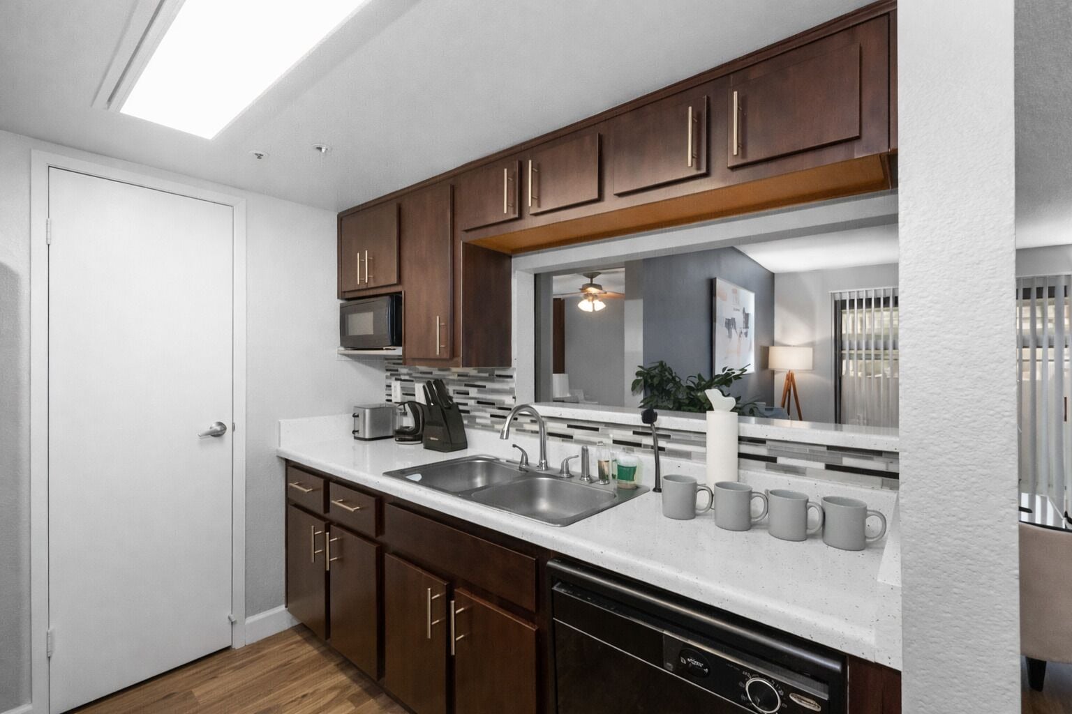 A compact kitchen with a microwave, toaster, and coffee maker on the countertop, a dishwasher below, and wooden cabinets above.