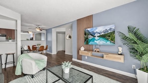 A modern living room with a flat-screen TV, a glass coffee table, and a large potted plant. - The Asteria by Stylish Stays (Tempe)