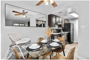 A modern dining area with a glass table, chairs, and a ceiling fan. - The Asteria by Stylish Stays (Tempe)