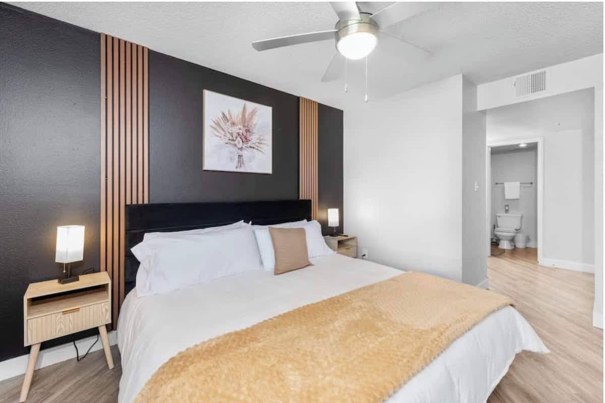 A bedroom with a bed, bedside tables, a ceiling fan, and a bathroom visible through an open door.