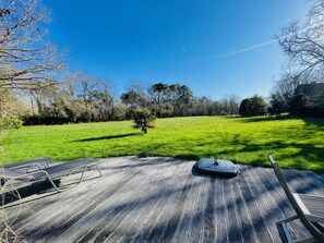 A wooden deck with a lawn chair and a table, overlooking a green field and trees. - Maison Familiale- Carnac & La Trinité (Carnac)