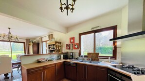 A kitchen with wooden cabinets, a built-in oven, a dishwasher, and a window with a view of the outdoors. - Maison Familiale- Carnac & La Trinité (Carnac)