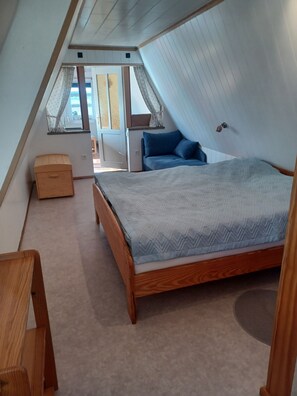 Ein Schlafzimmer mit schrägem Dach, einem Bett, einer hölzernen Bank und einem Fenster mit Vorhängen.