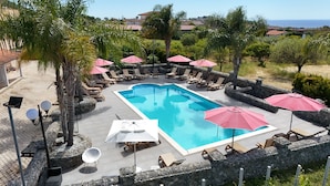 Une piscine rectangulaire entourée de murs de pierre et de palmiers, avec des chaises longues et des parasols.