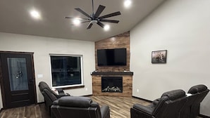 A modern living room with a fireplace, leather sofas, a flat-screen TV, and a ceiling fan. - Gorgeous rustic modern home tucked away in Texarkana - 4 bedrooms available (Texarkana)