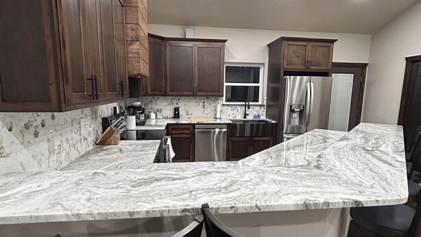 A kitchen with dark wooden cabinets, a marble countertop, stainless steel appliances, and bar stools. - Gorgeous rustic modern home tucked away in Texarkana - 4 bedrooms available (Texarkana)