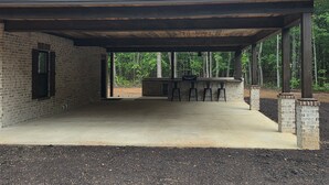 A covered outdoor patio with a brick wall, a metal roof, and a bar area with stools. - Gorgeous rustic modern home tucked away in Texarkana - 4 bedrooms available (Texarkana)
