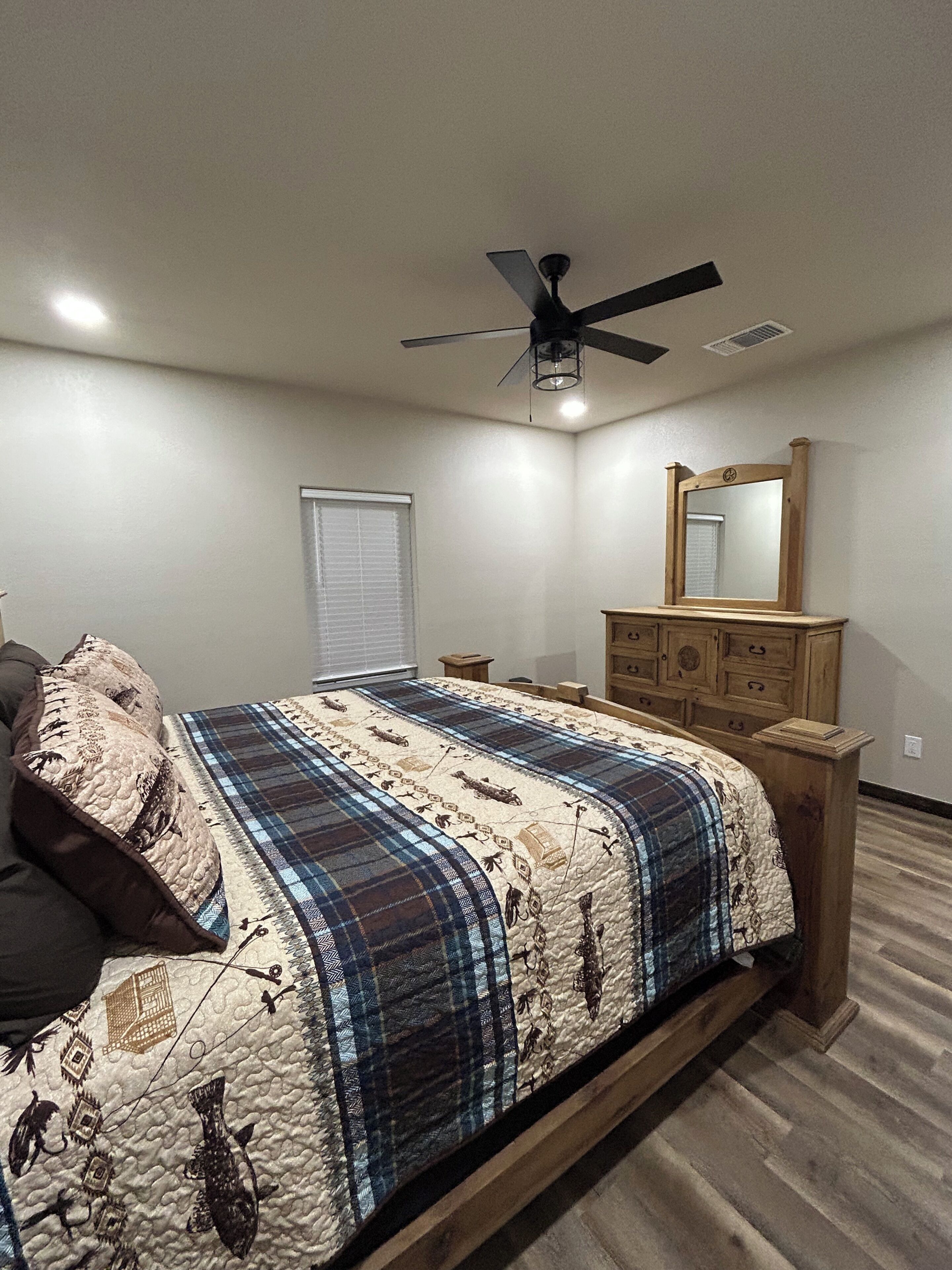 A bedroom with a bed, a ceiling fan, a dresser, and a window with blinds.