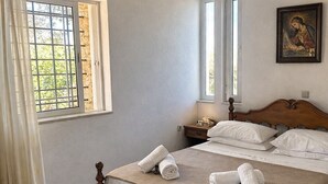 Ein ordentlich bezogenes Bett, gerollte Handtücher, eine Pendelleuchte, ein Bild an der Wand und ein Fenster mit Vorhängen.