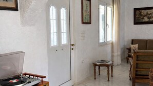 Ein Zimmer mit einer weißen Tür, einem Holzschrank mit Plattenspieler, einem kleinen Tisch, einem braunen Sofa und einem Gemälde an der Wand.