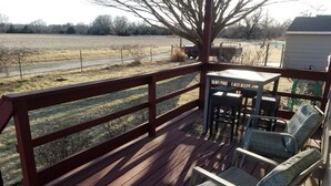 A wooden deck with a railing, outdoor furniture, and a view of a field.
