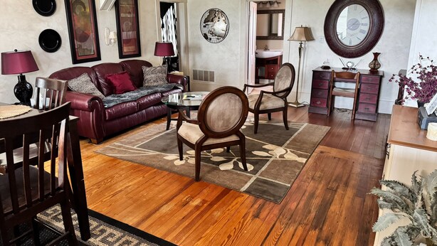 A living room with a leather sofa, wooden chairs, a dining table, and a ceiling fan.