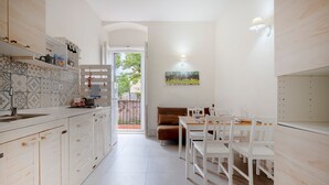 Eine moderne Küche mit weißen Schränken, ein Essbereich mit weißen Stühlen und ein braunes Sofa.