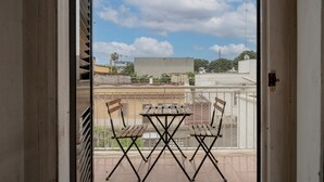 Ein Balkon mit Tisch und zwei Stühlen, Blick zum Himmel und ein Gebäude im Hintergrund.