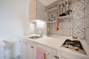 A kitchen with a sink, stove, and shelves with kitchen items. - Studio 'Garibaldi54 - Camera del Fico' with Balcony, Wi-Fi and Air Conditioning (Bari)