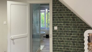 Una habitación con una puerta blanca, un panel de vidrio, un muro de ladrillo y vistas al exterior.