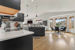 Une cuisine moderne avec des meubles de couleur sombre, un îlot central et des luminaires suspendus.