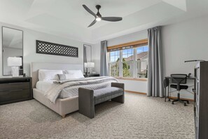 Un dormitorio con cama, mesitas de noche, escritorio, silla, ventilador de techo y ventana con cortinas.