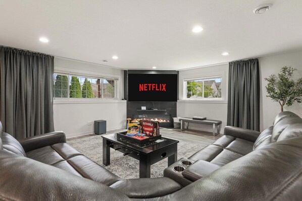 Una sala de estar moderna con una televisión de pantalla plana, sofás de cuero, una mesa de centro con juegos de mesa y una chimenea.