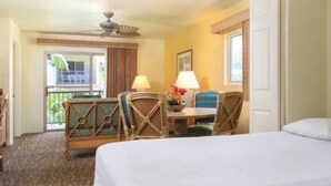 A hotel room with a bed, a desk with two chairs, a ceiling fan, and a view of the outdoors. - Cozy 1-bedroom fully furnished condo sleeps 4 in serene Kailua-Kona with AC (Kailua-Kona)
