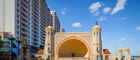 A historic stone archway with a large central arch, flanked by two towers, leading to a modern high-rise hotel.