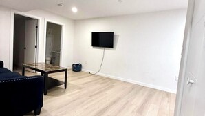 A room with a flat-screen TV mounted on the wall, a dark blue sofa, a wooden coffee table, and a light wooden floor. - Peaceful Family Home | 4BR, Huge Deck, Garage & Free Wi-Fi (Winnipeg)