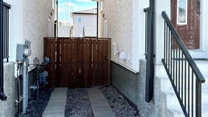 A narrow pathway leading to a gated entrance with a wooden fence, a concrete pathway, and a small gravel area. - Peaceful Family Home | 4BR, Huge Deck, Garage & Free Wi-Fi (Winnipeg)