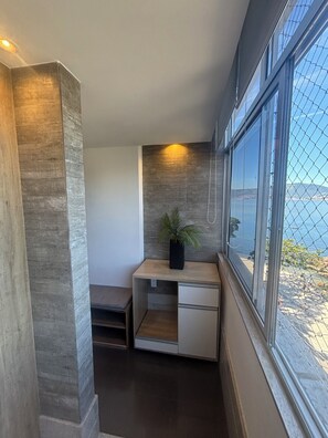 A corner room with a desk, a potted plant, a window with a view of the sea, and a textured wall. - Beachfront apartment with a spectacular view of Flexas beach!! (Niterói)