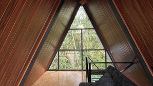 An attic room with wooden walls, a window, and a sofa. - Refugio de la Niebla Puyo Glamping (Puyo)